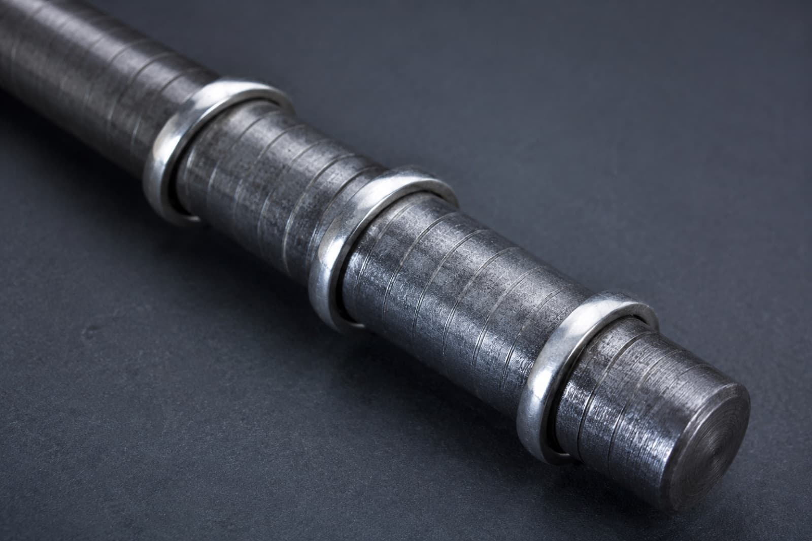A steel ring sizing mandrel with three plain silver bands slid onto it at different heights